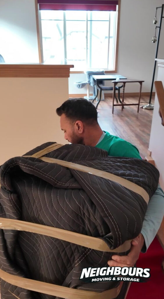 Professional Neighbours Moving & Storage mover carefully carries a furniture piece protected with moving blankets for safe, damage-free transport during a residential move.