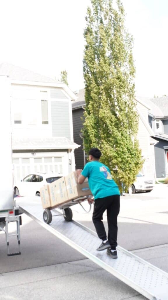 Moving professional loading boxes onto a truck with a ramp in a suburban neighborhood.