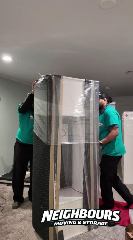 Movers handling a large glass display case for storage or transport.